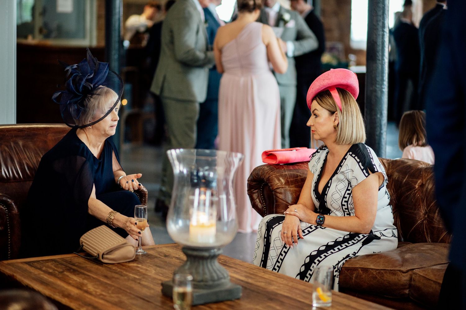 Two guests chatting on a brown leather couch during a wedding reception.