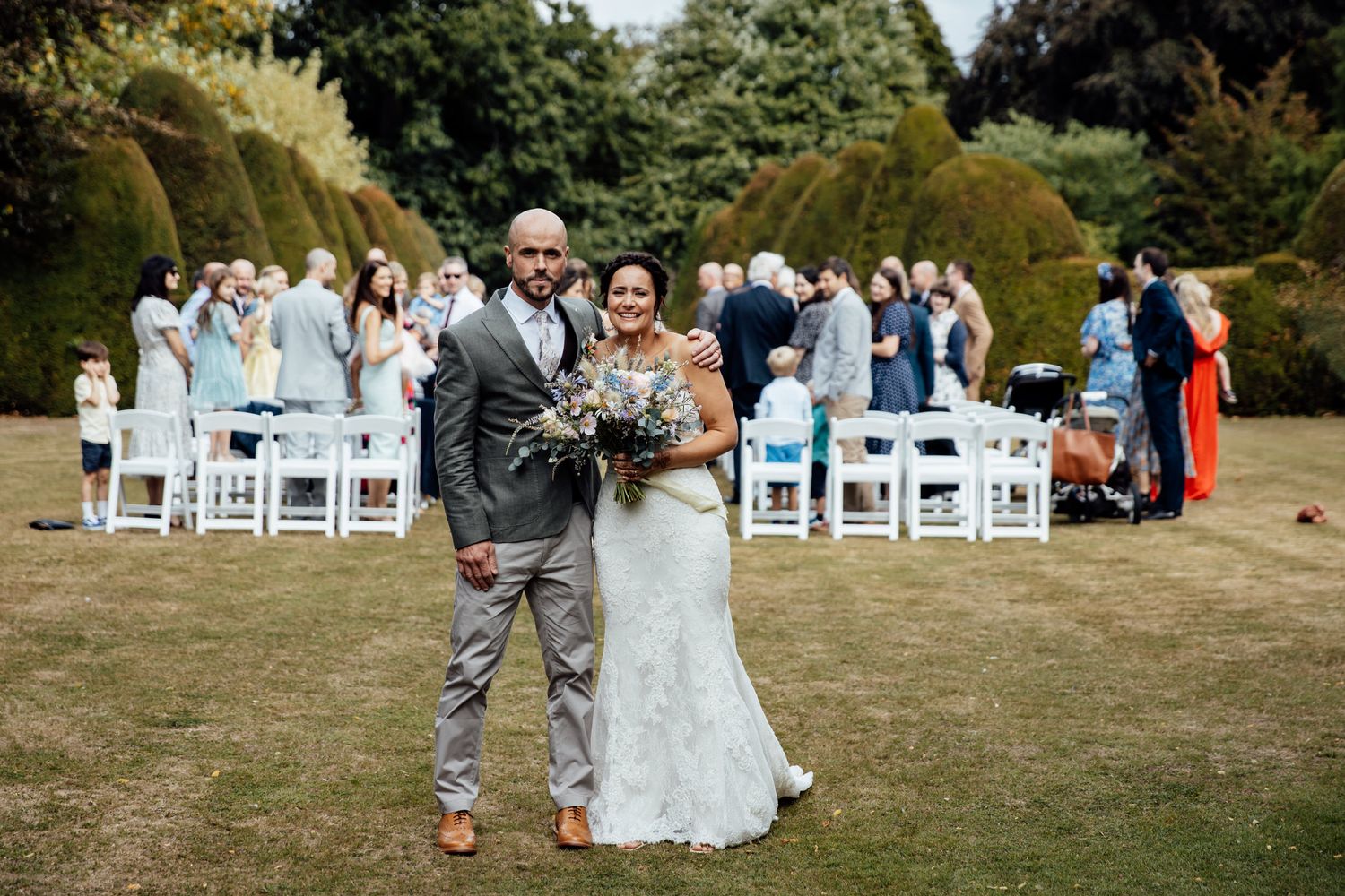 Outdoor wedding ceremony setup with white chairs on a lawn near historic buildings.