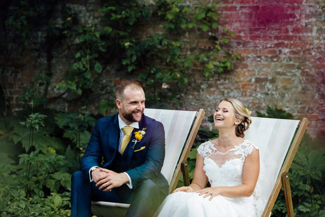 Wedding couple relaxing in deck chairs against an ivy-covered brick wall.