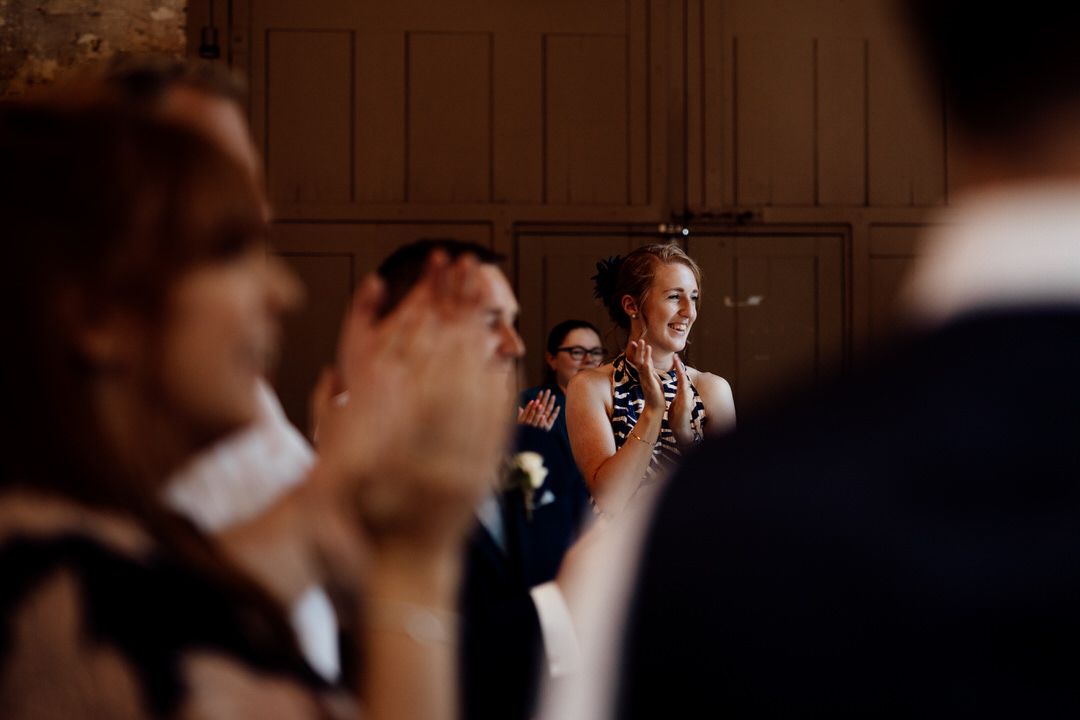 Wedding guests celebrate in a dimly lit rustic indoor venue.
