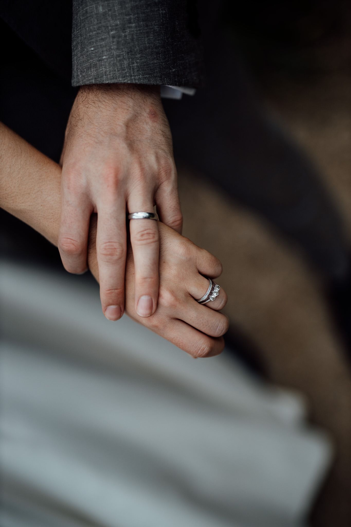 Close-up shot of wedding rings on hands against a gray background.