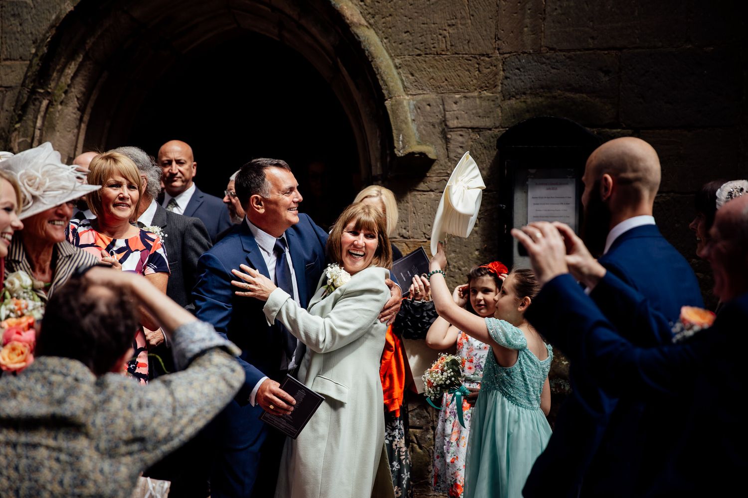 Wedding guests celebrate with raised hands under stone archway.