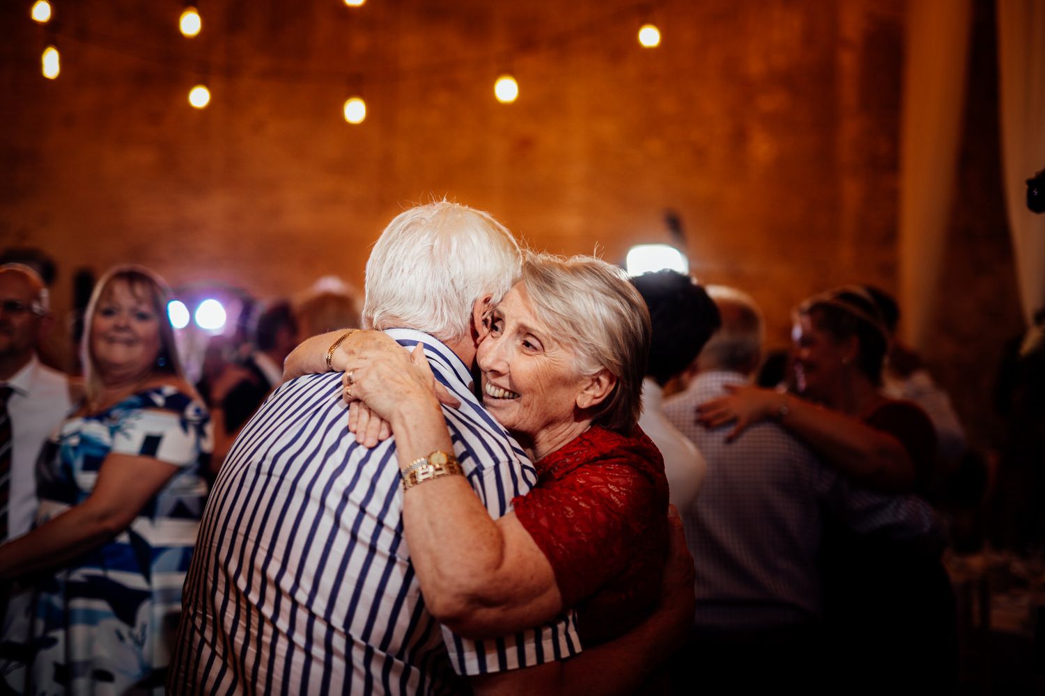 Wedding guests dancing and celebrating on a lively dance floor with string lights overhead.