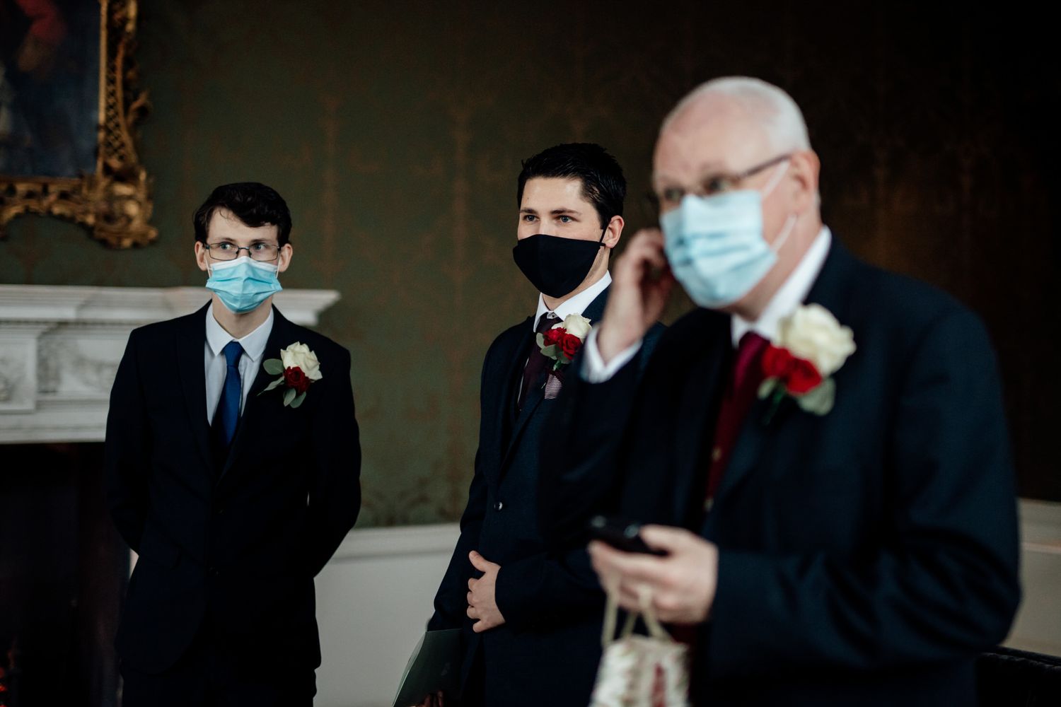 Wedding guests in formal attire wearing protective masks during ceremony.