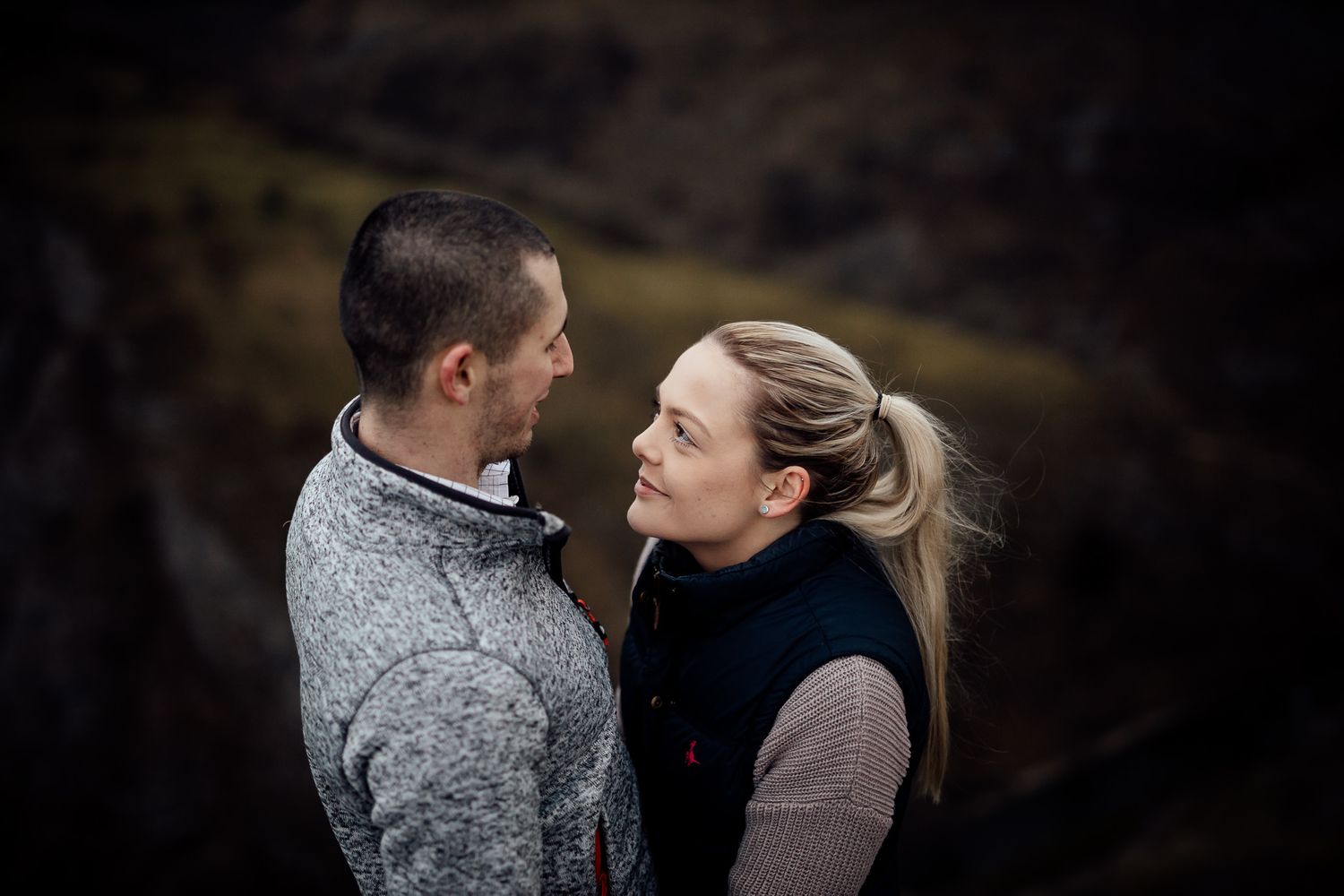 Two people share a tender moment against a dramatic dark mountain backdrop.