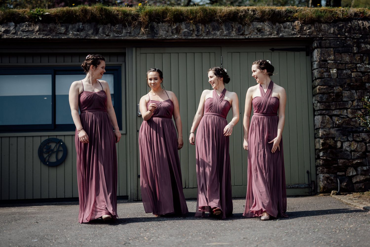 Bridesmaids in dusty rose dresses lined up against stone wall.