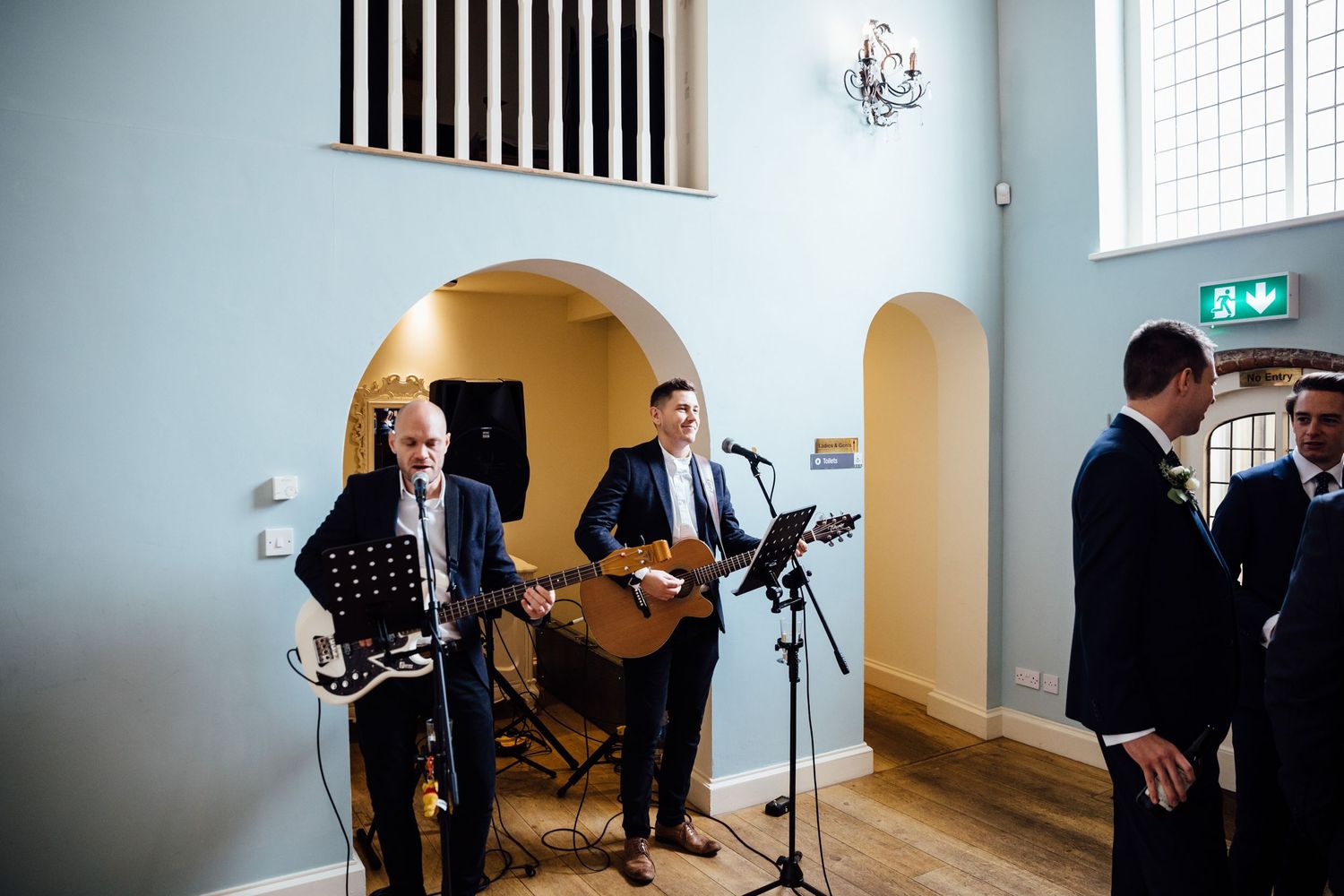 Musicians setting up equipment in a minimalist white room with striped wall accents.
