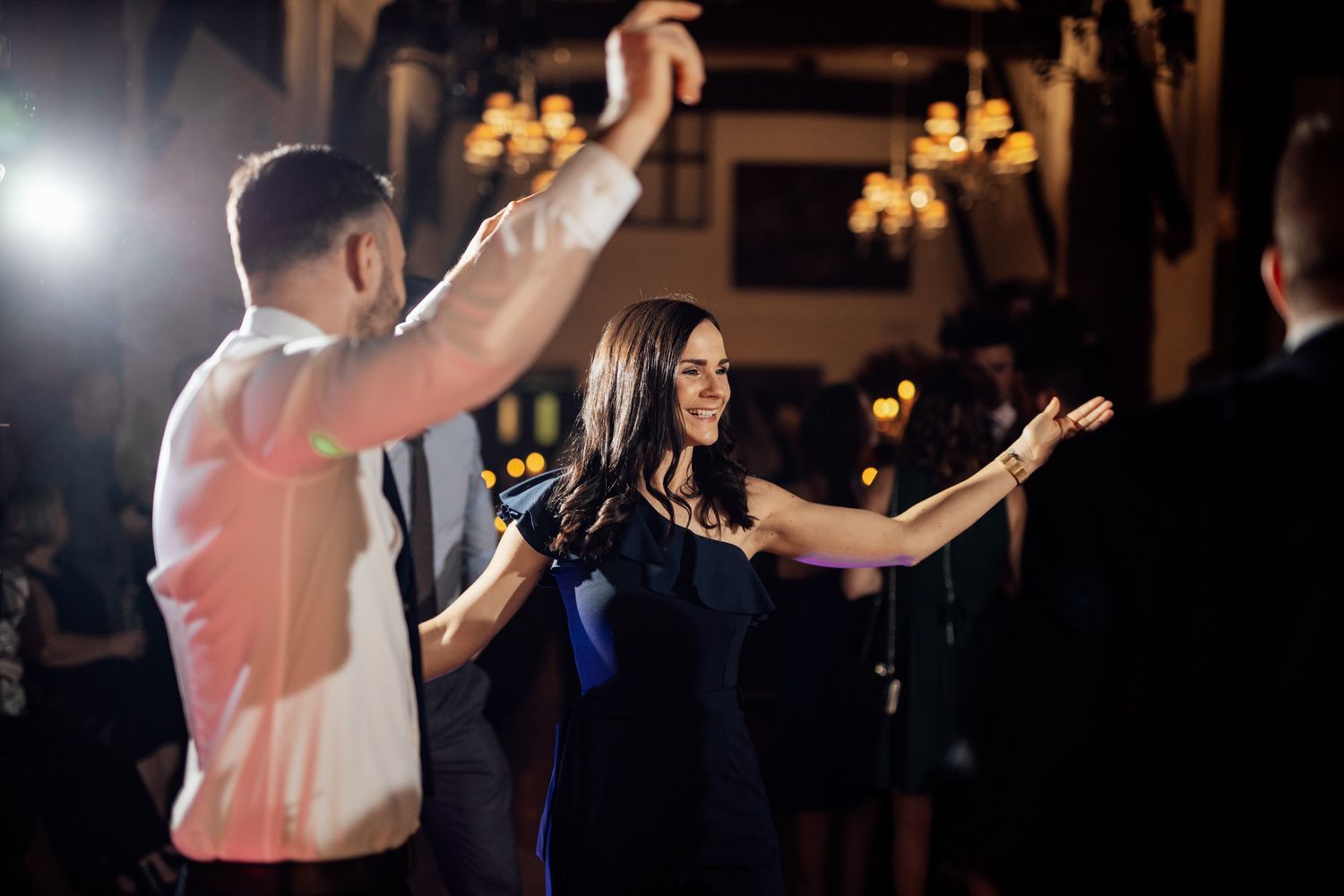 Guests dancing together at an elegant evening reception with warm lighting and chandeliers overhead.
