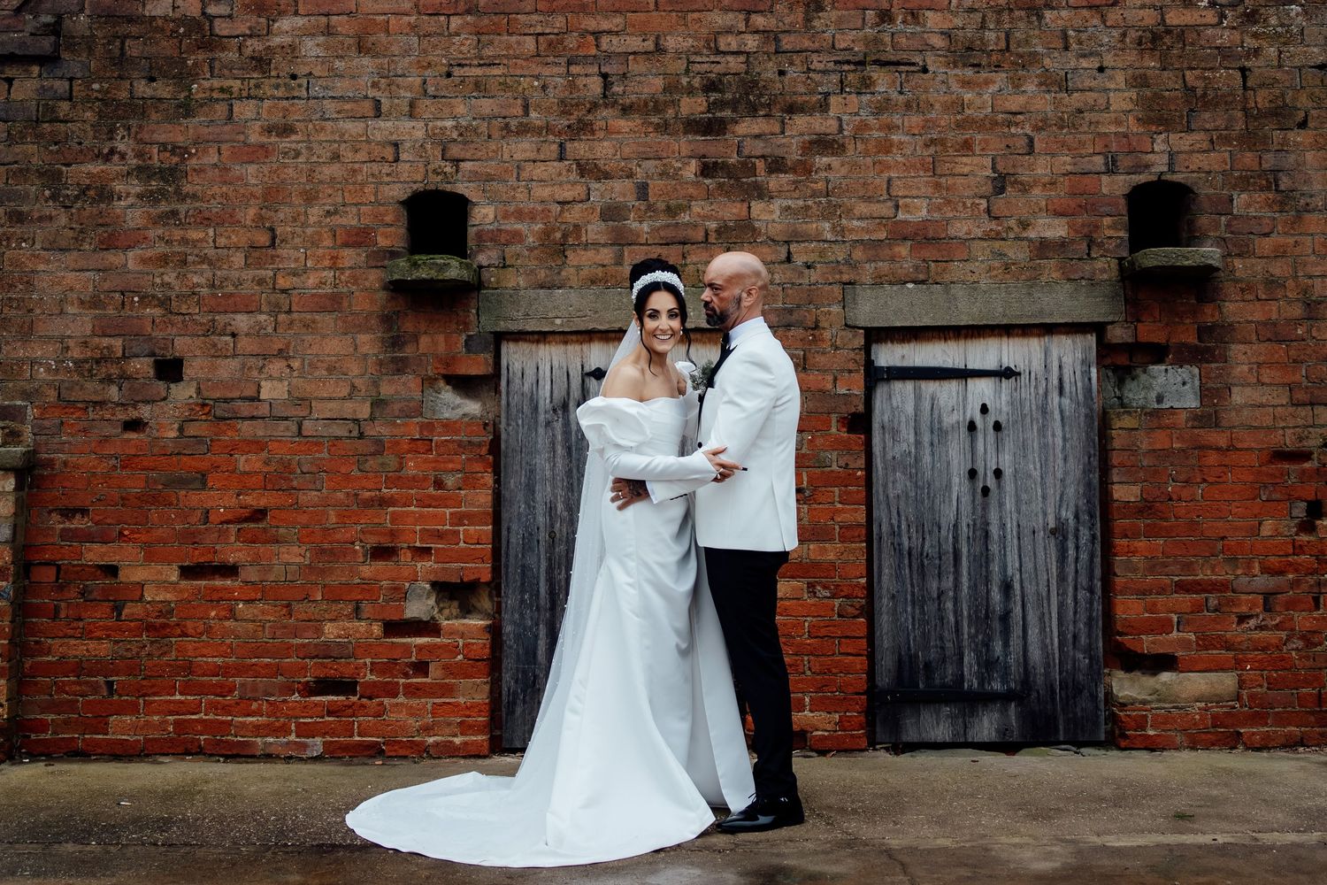 A couple poses for portraits against a rustic brick wall backdrop.
