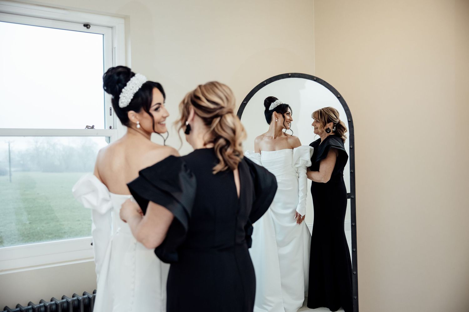Wedding party members in formal attire gather together in a bright room before the ceremony.