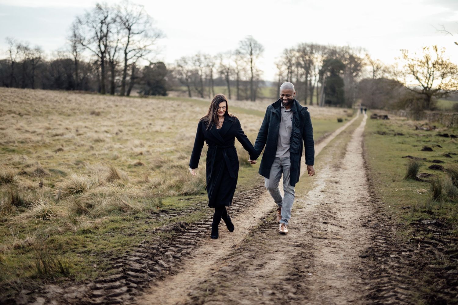 A couple walks together on a winding dirt path through a serene autumn countryside landscape.