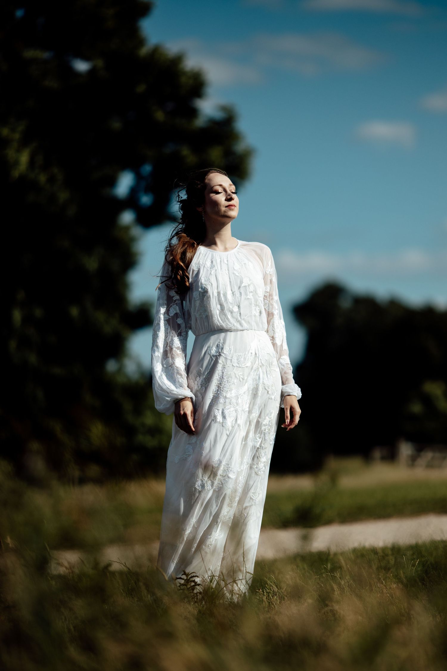 A dreamy portrait series in a field shows a flowing white lace dress catching sunlight against a natural landscape.