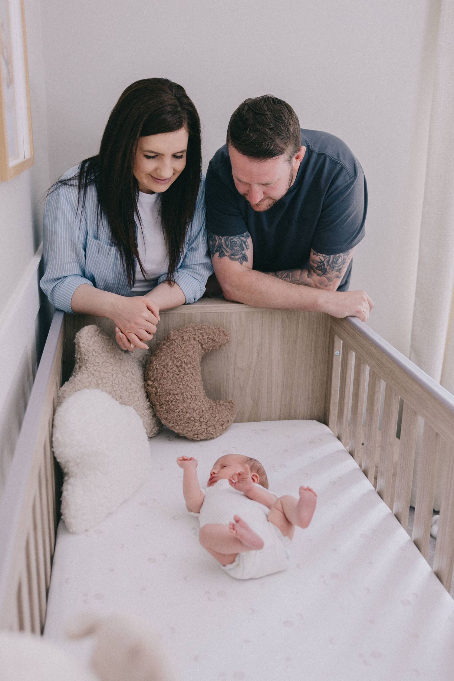 Parents lovingly gazing at their newborn baby lying in a wooden crib with stuffed animals in a nursery.