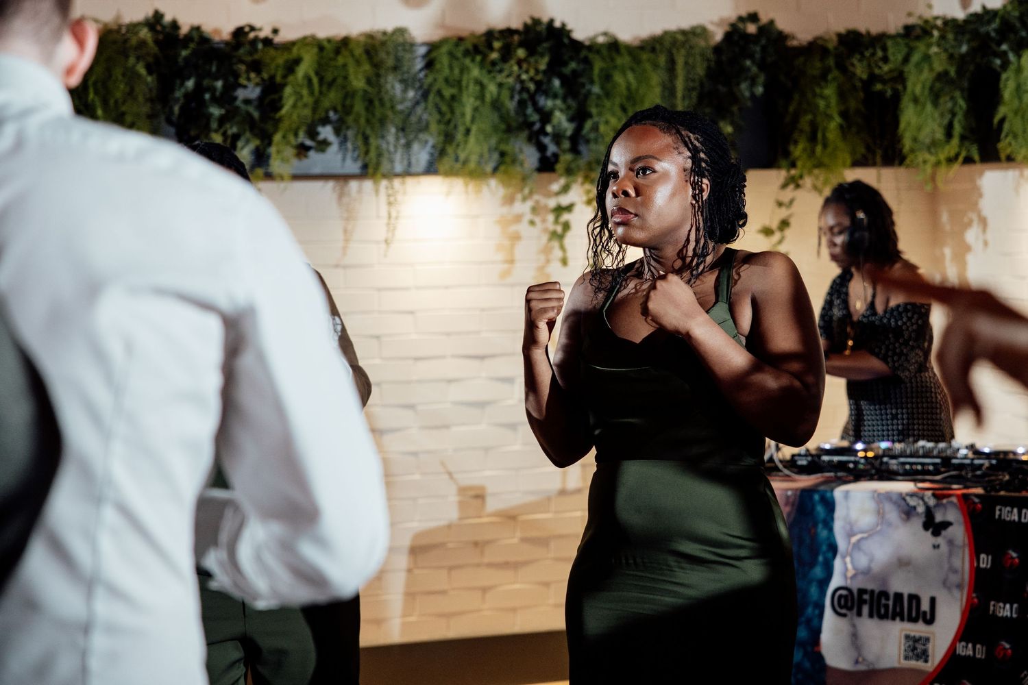 Wedding guest in black dress dancing energetically near DJ booth at lively reception.