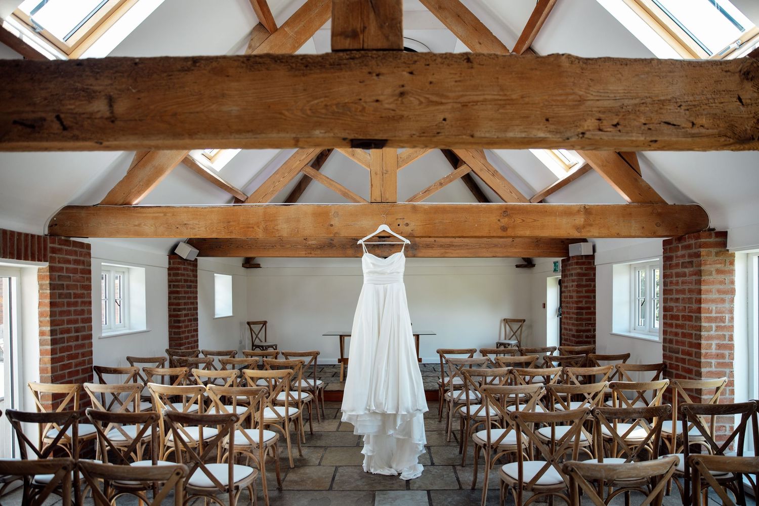 Empty rustic wedding ceremony venue with wooden cross-back chairs and exposed beams.
