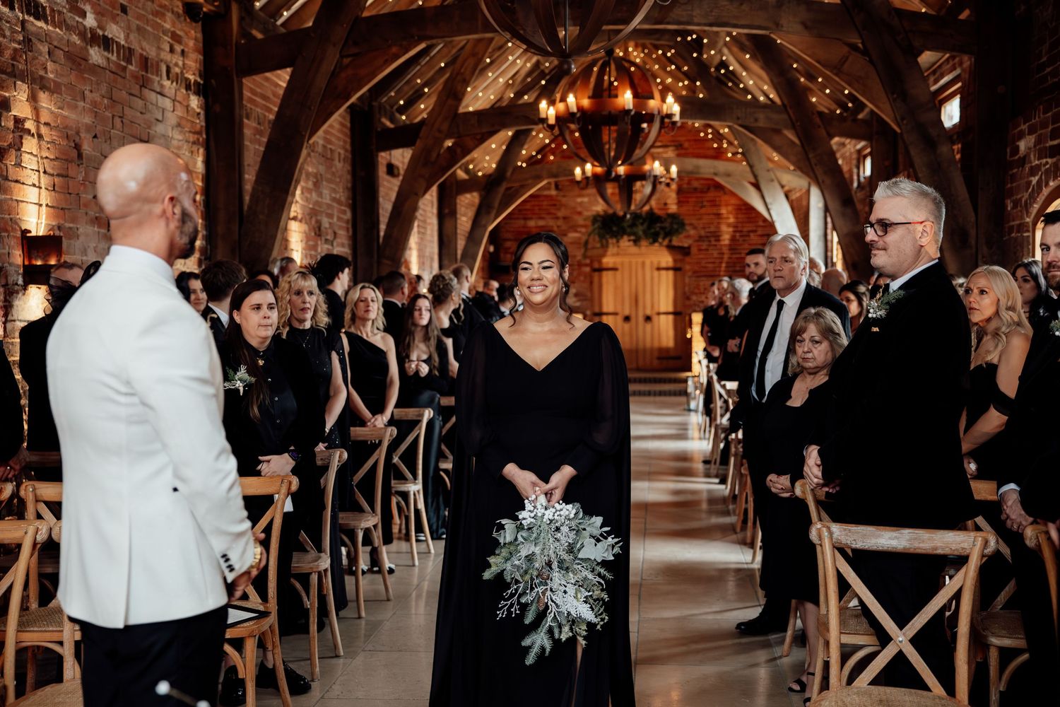 Elegant wedding ceremony setup in rustic brick venue with cross-back chairs and romantic lighting.