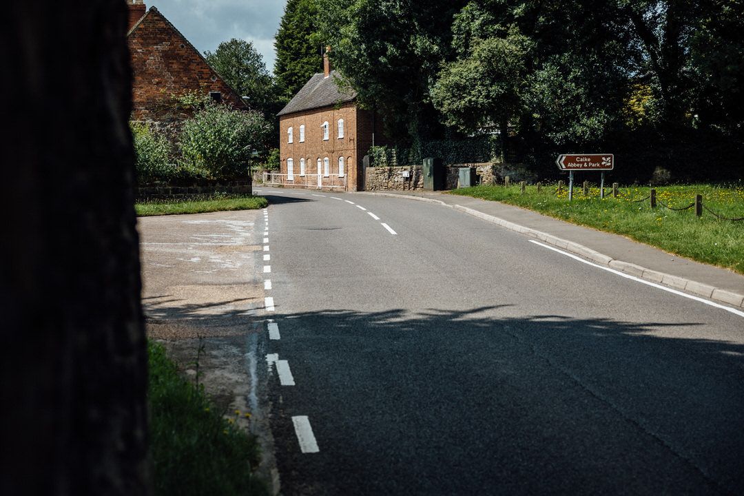 Rural country road leading to small brick church building surrounded by trees.