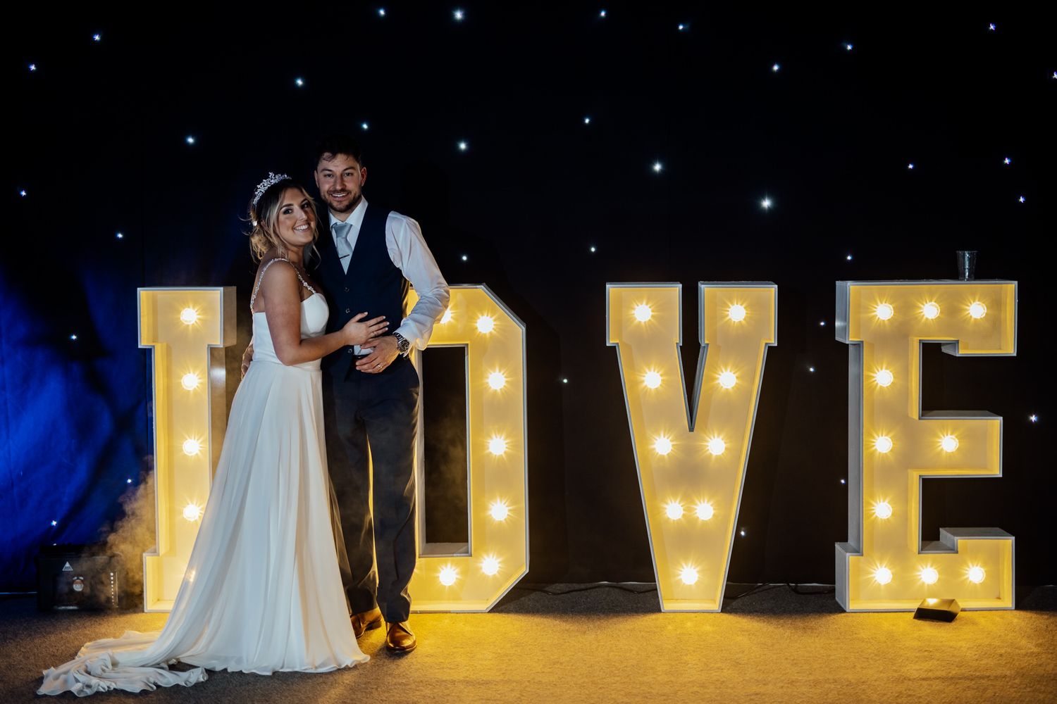 Illuminated LOVE marquee letters create a romantic backdrop for an evening wedding celebration.