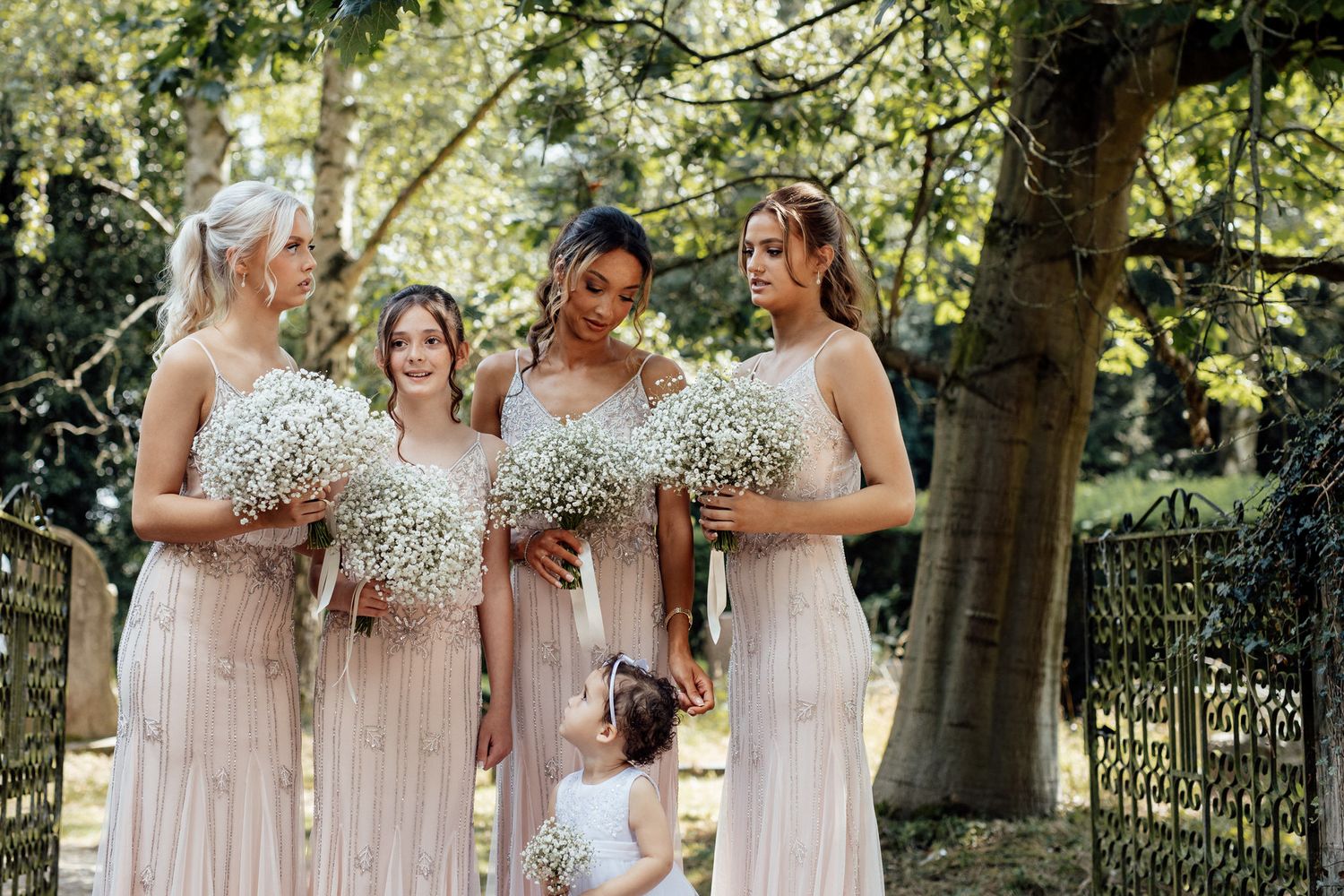 Bridesmaids in soft pink dresses gather together in garden setting.