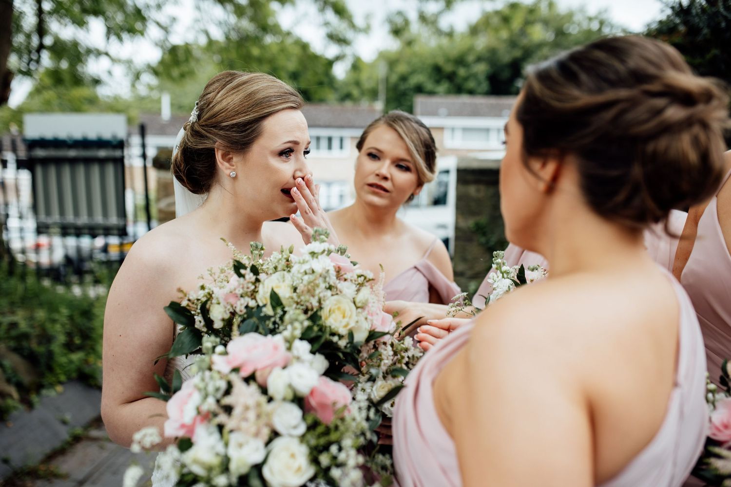Wedding party members sharing joyful moments while holding white and pink floral bouquets.