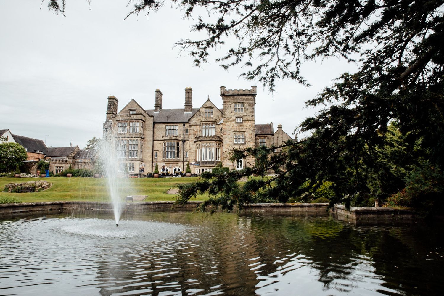 Scenic mansion wedding venue with fountain and lake reflecting historic stone architecture.