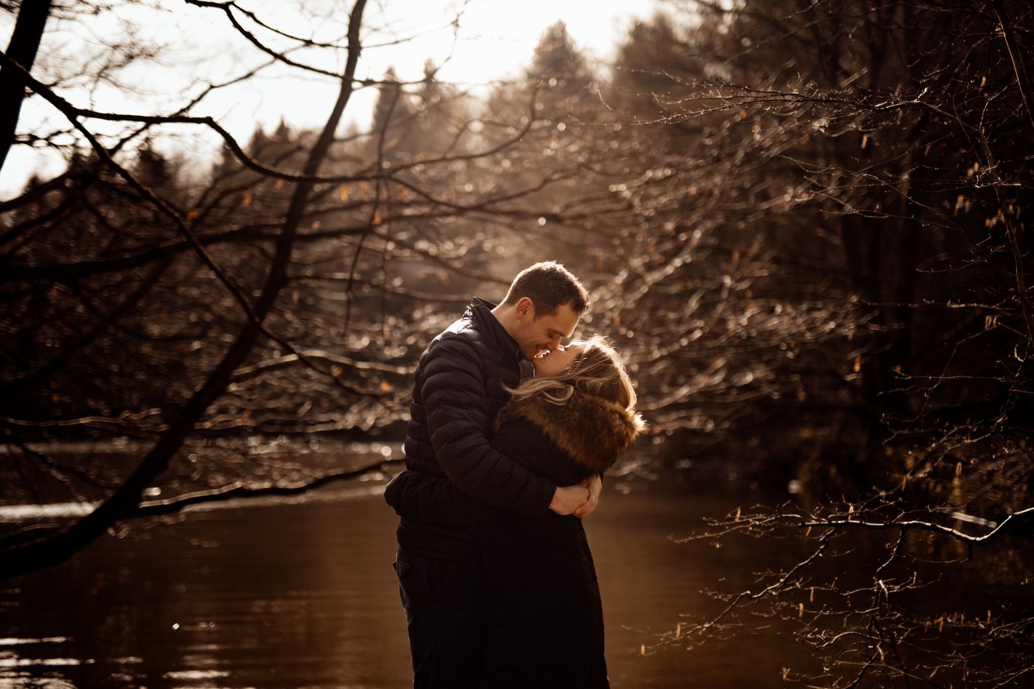 Silhouetted figures embrace against a moody winter forest backdrop with bare branches.