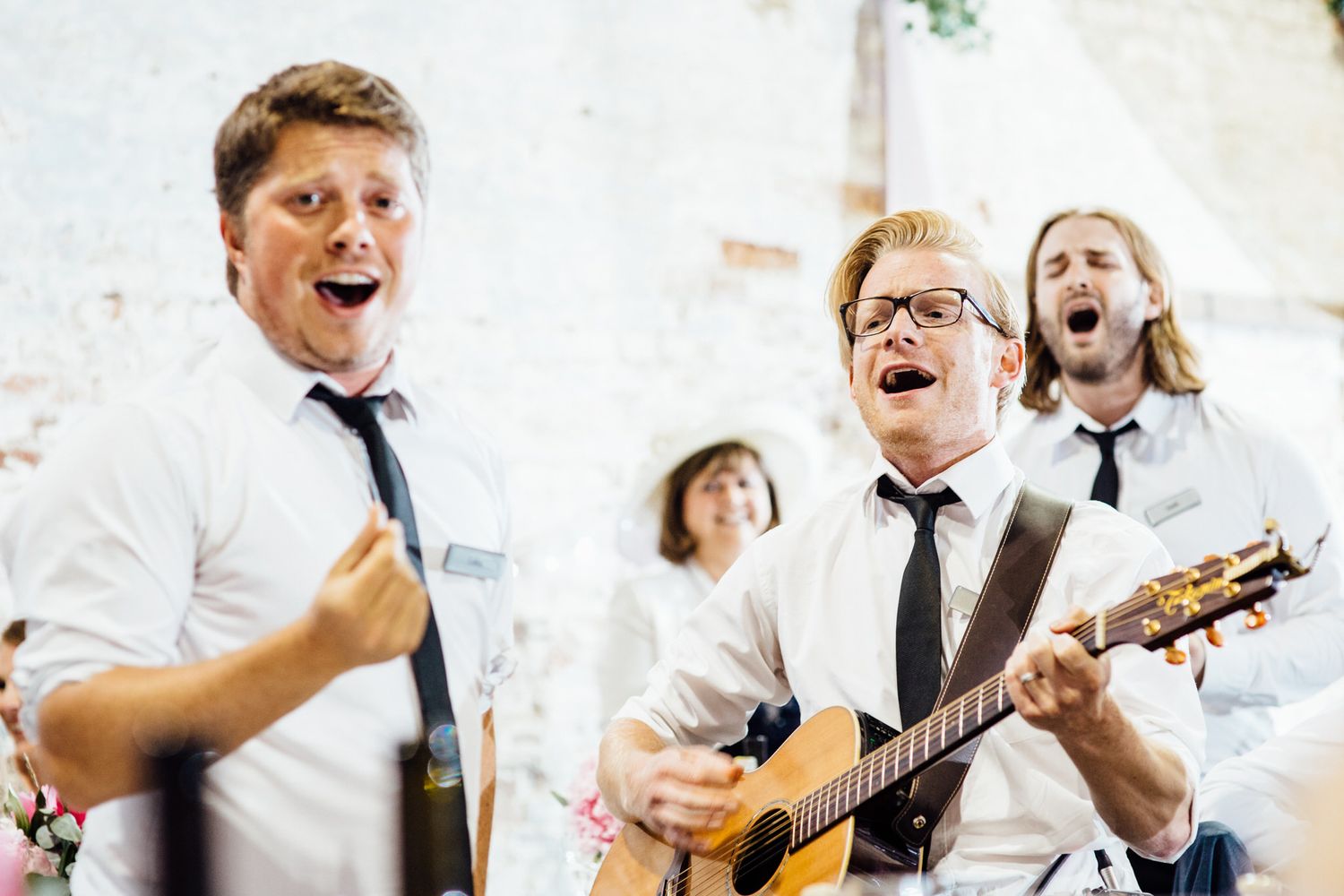 Musicians performing and singing with guitars at an indoor wedding reception.