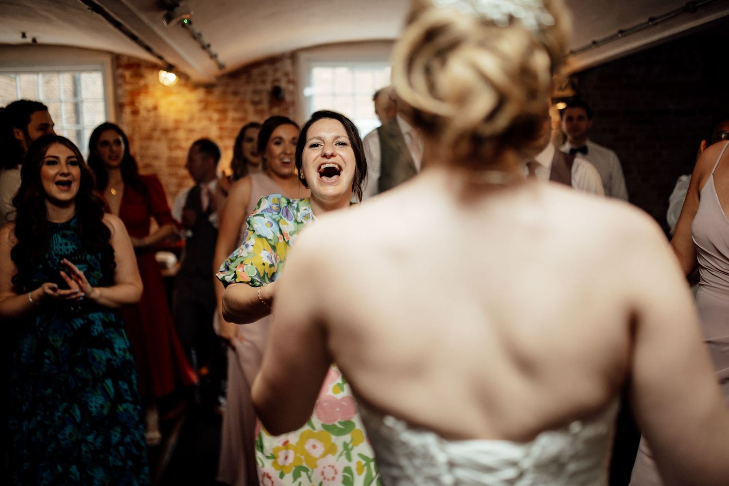 Candid moments of celebration and laughter during a wedding reception with brick wall backdrop.