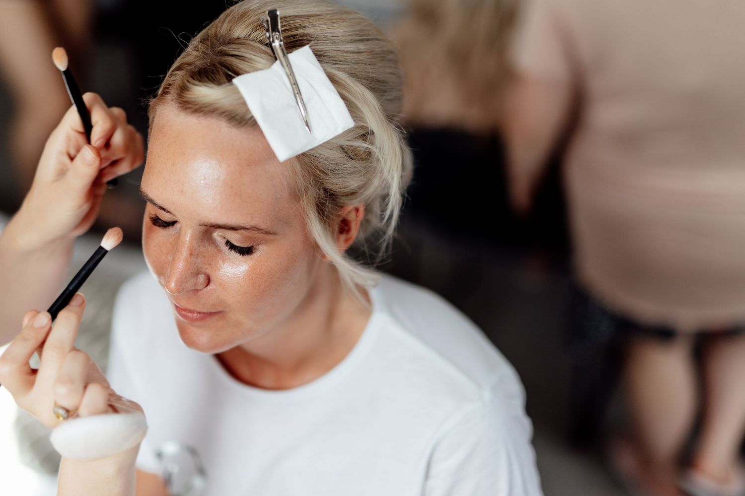 Wedding preparation scene with makeup and styling in natural window light.