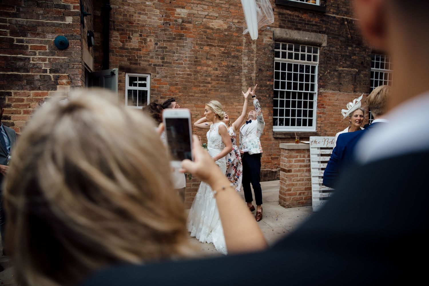 Candid wedding moments captured against rustic brick wall backdrop.