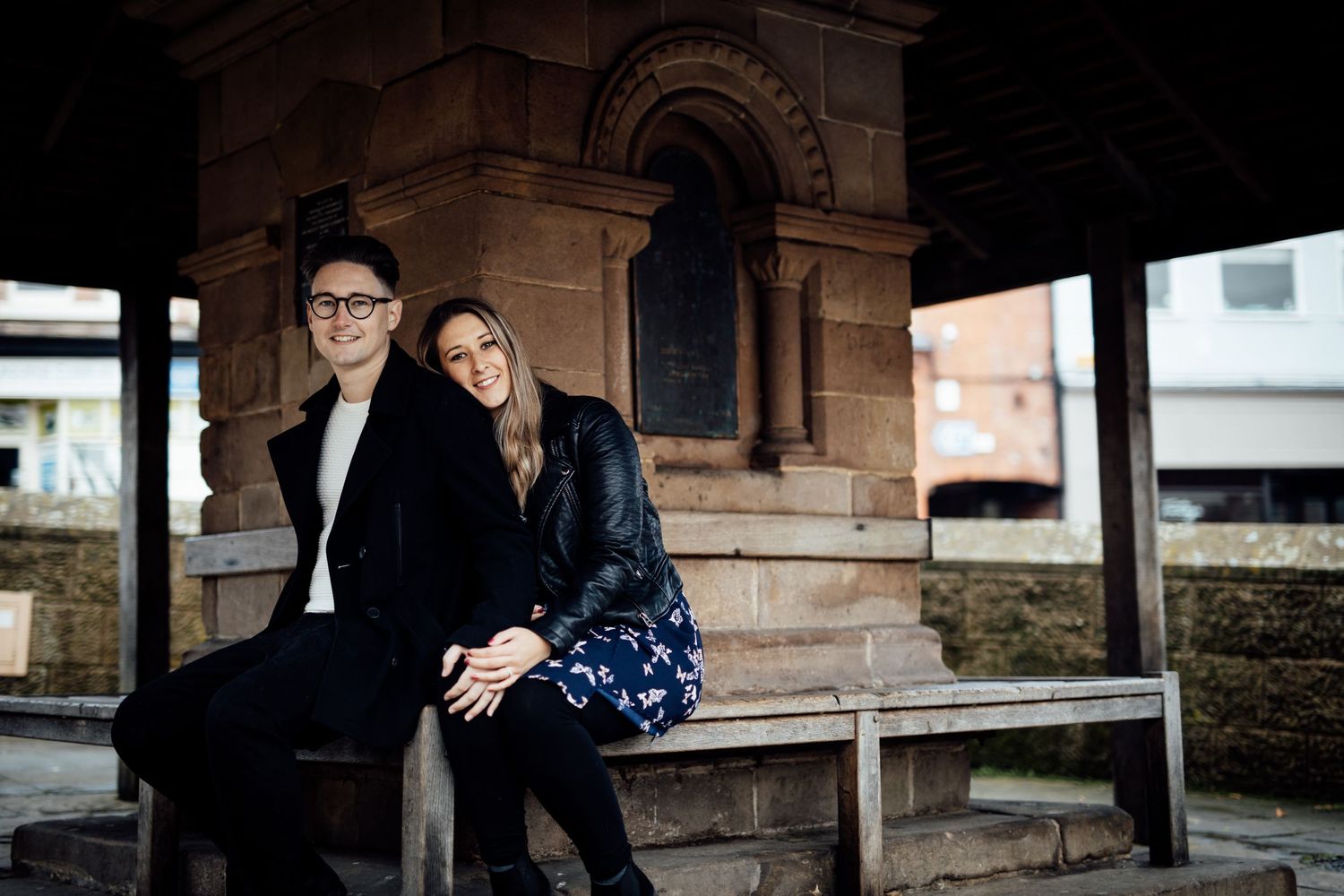 Couple poses under stone colonnade during romantic outdoor session.