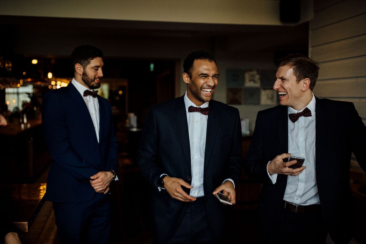 Three groomsmen in tuxedos sharing a laugh during wedding celebrations.
