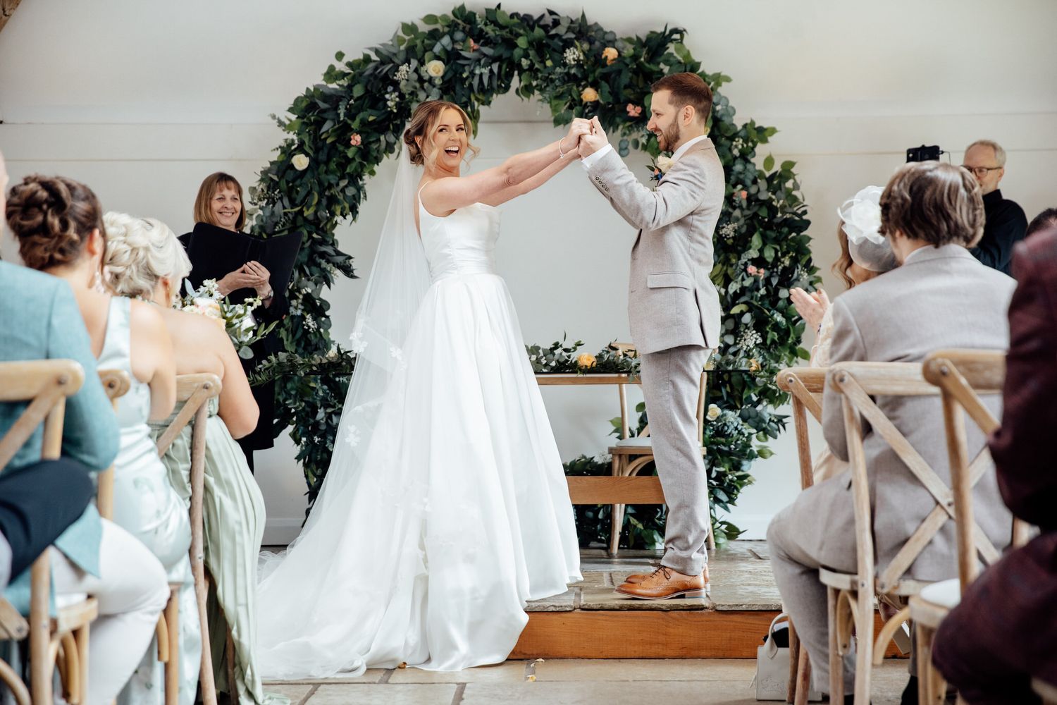 A celebratory moment during a wedding ceremony under a floral arch with guests watching.