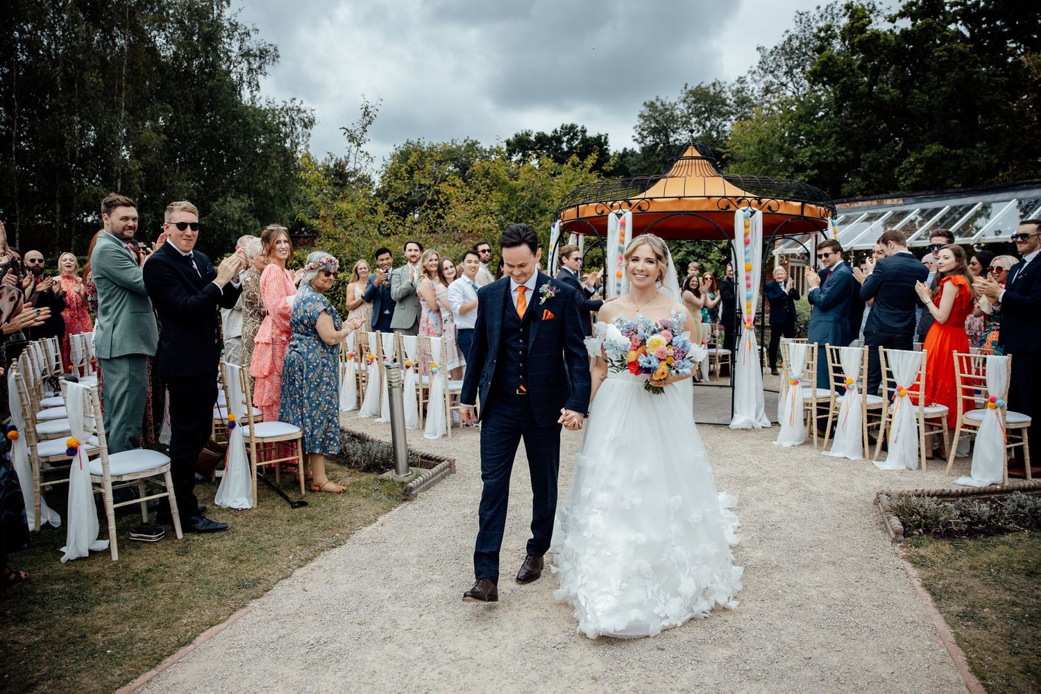 Wedding ceremony procession on a gravel path with guests watching from both sides.