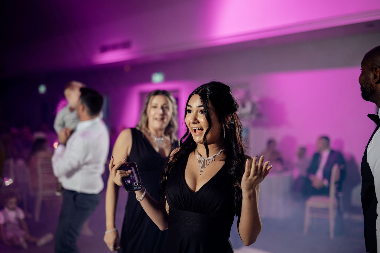 Guest dancing enthusiastically at wedding reception under purple mood lighting.