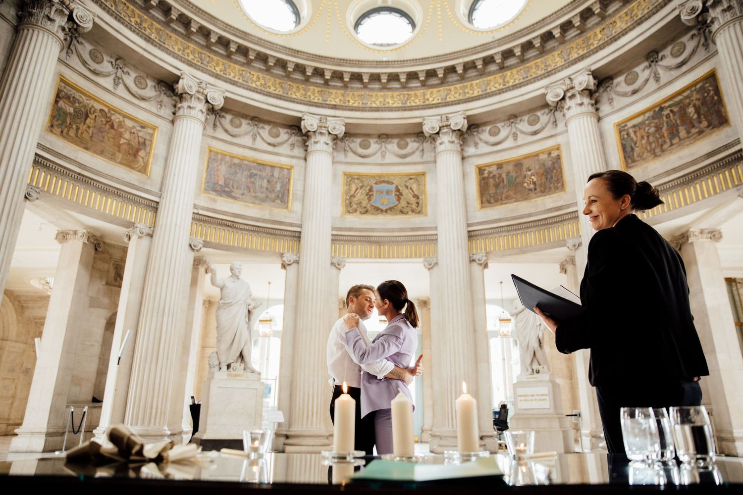 Wedding ceremony in grand domed hall with classical architecture and columns.