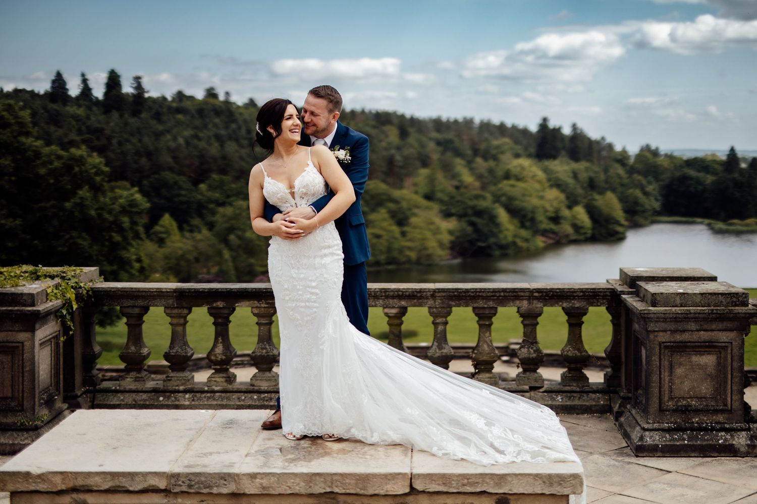 A romantic wedding portrait on a stone balcony overlooking a scenic lake view.