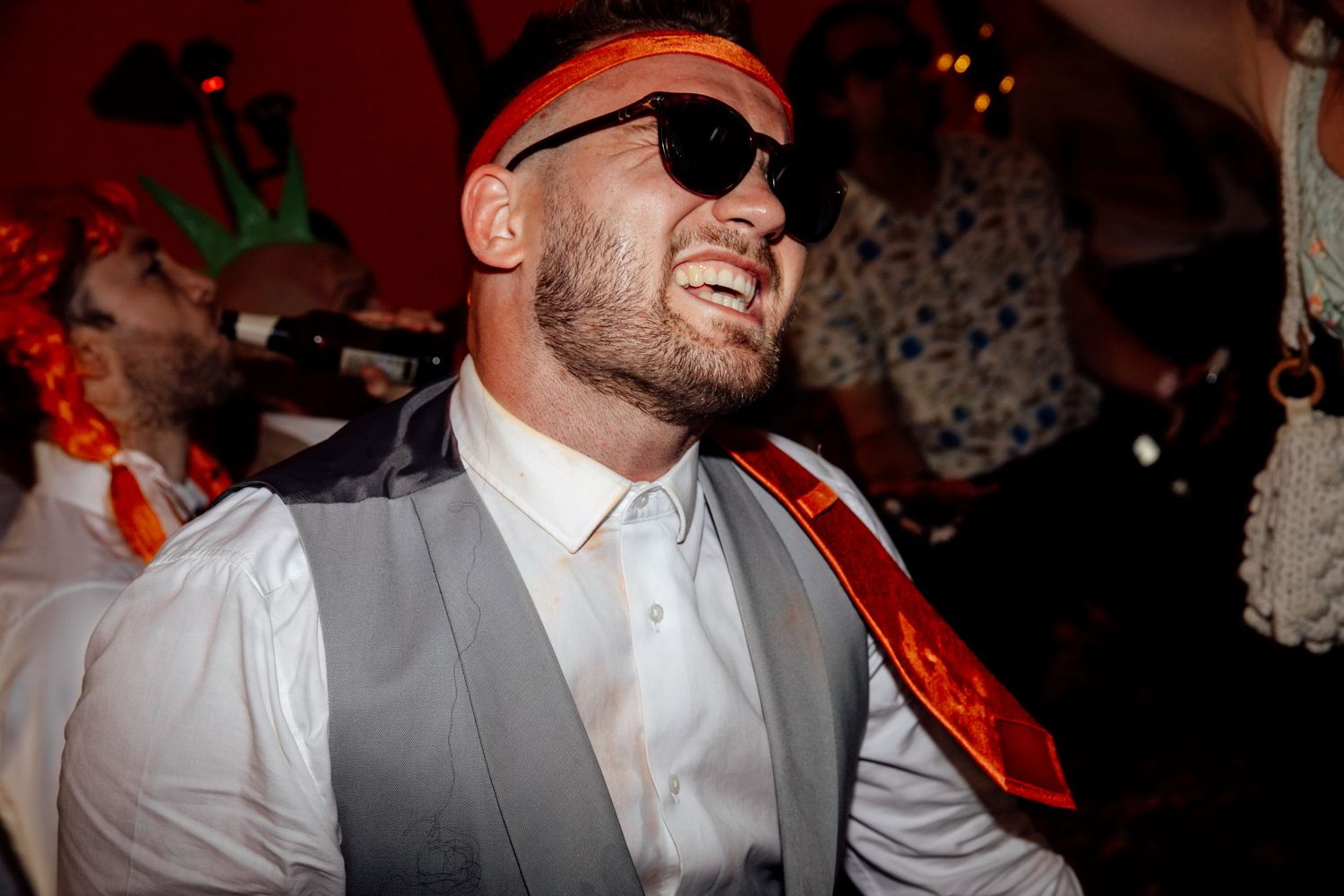 Party atmosphere with person wearing sunglasses and vest under red lighting.