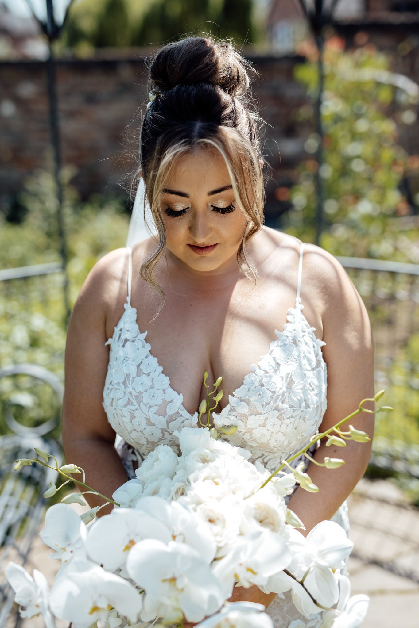 Bride with elegant updo hairstyle holding white orchid bouquet in natural lighting.