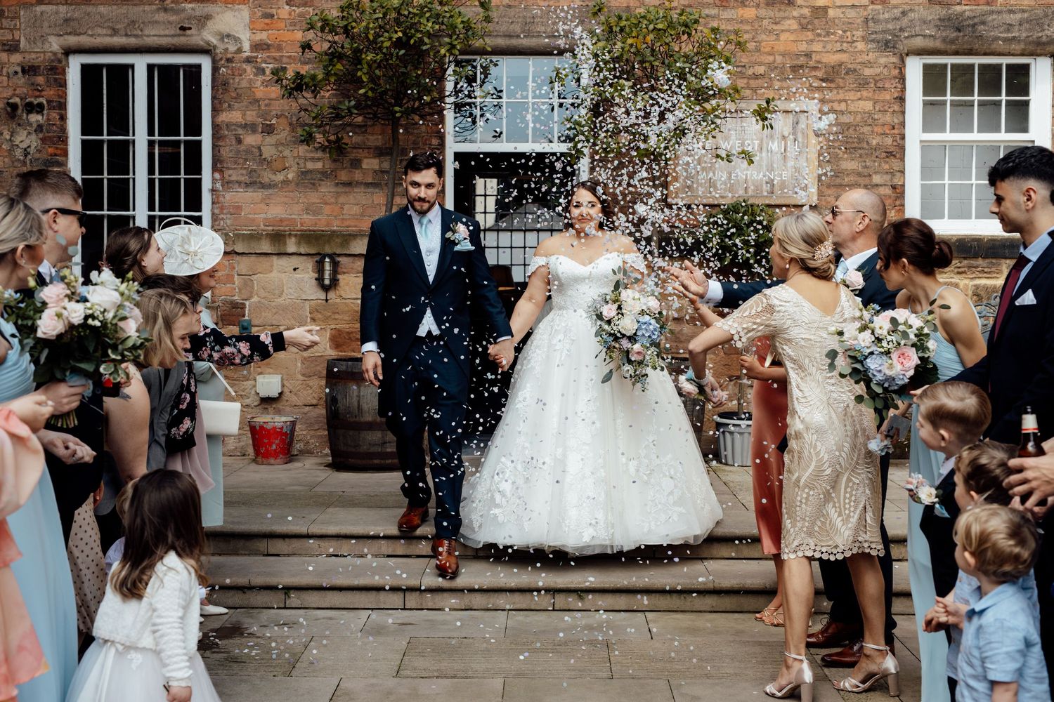 Wedding celebration outside historic brick building with guests throwing confetti.