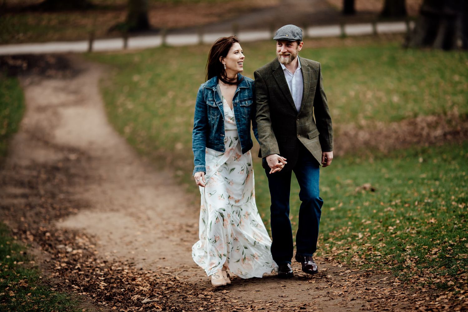A couple walks hand in hand along a winding dirt path through a park.