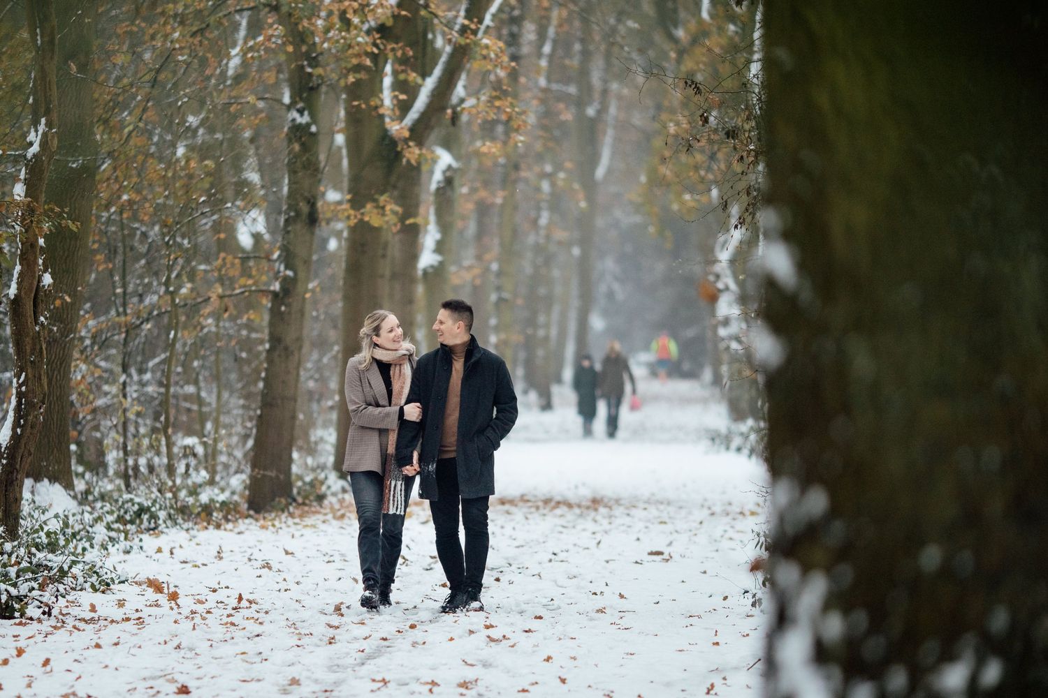 A couple takes a romantic winter walk along a snowy path through a forest.