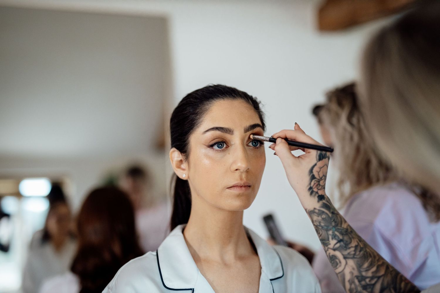 Wedding preparation scene with makeup artists working in a bright room.