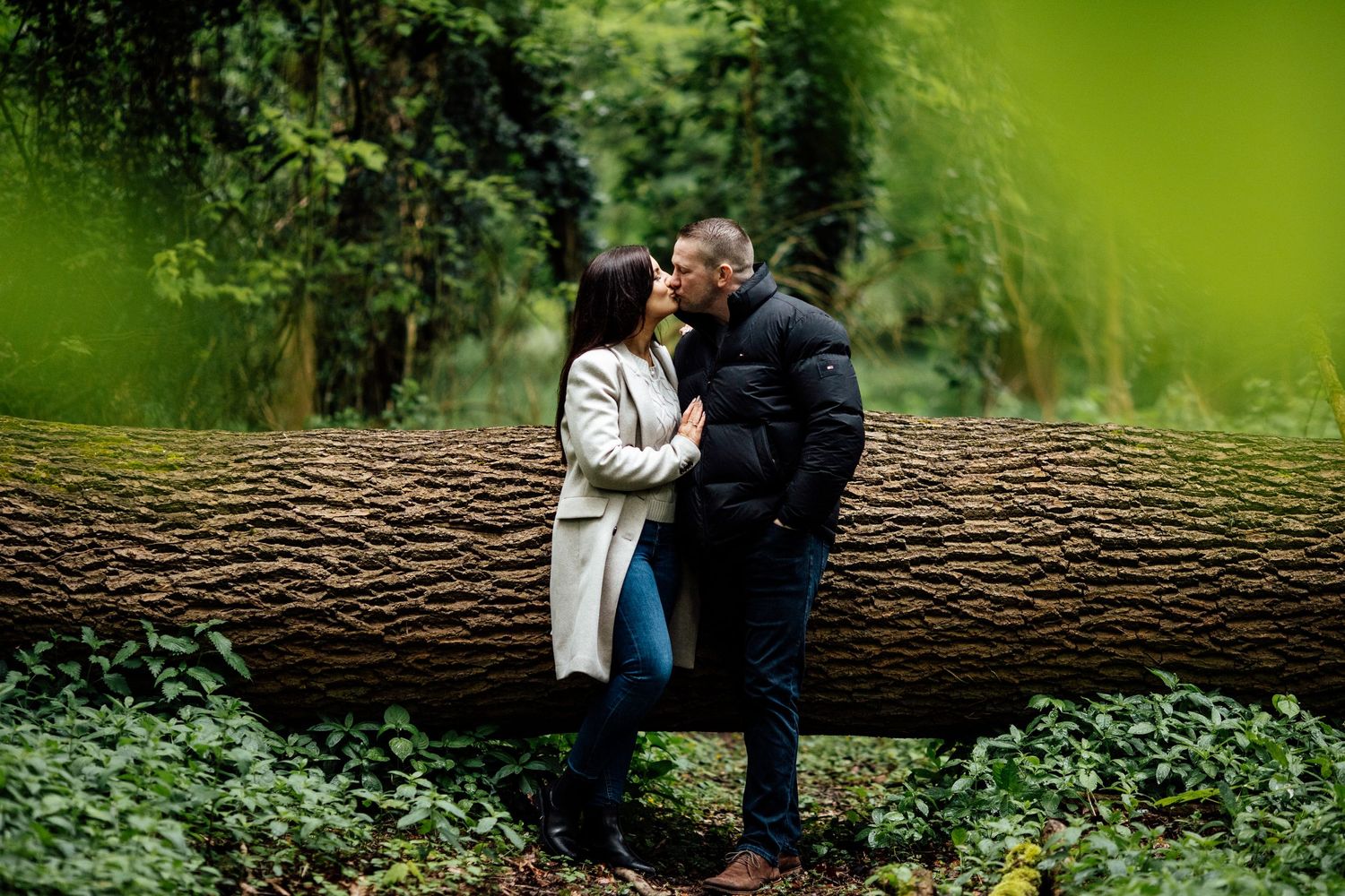 Two people sit together on a fallen log in a verdant forest setting.