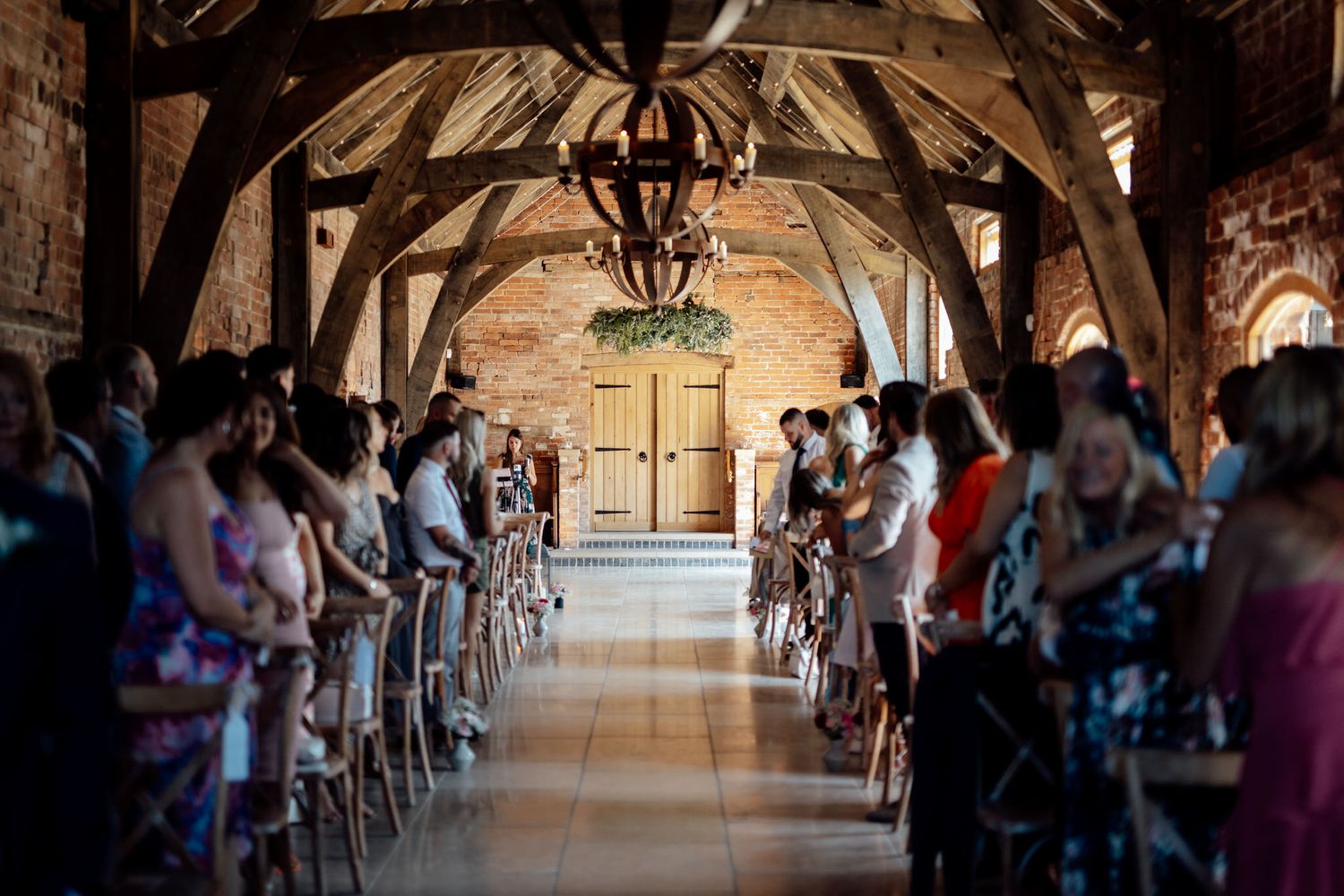Wide angle view of rustic wedding ceremony venue with arched ceiling and guests seated.