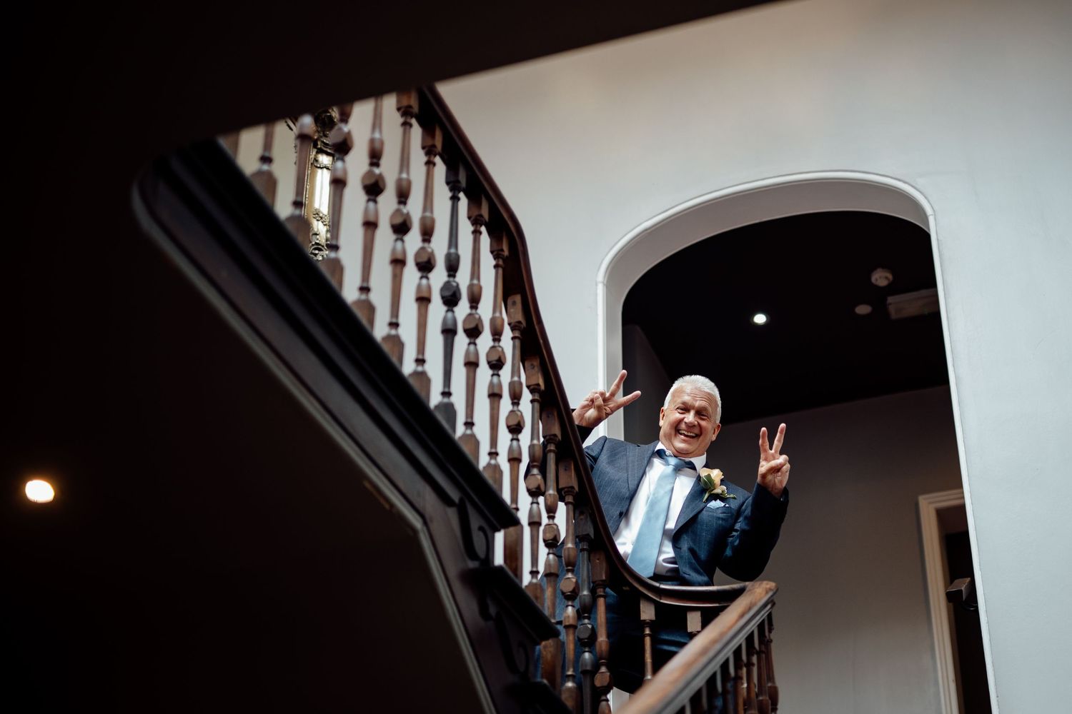 Person in formal attire making peace sign while posing on elegant staircase.