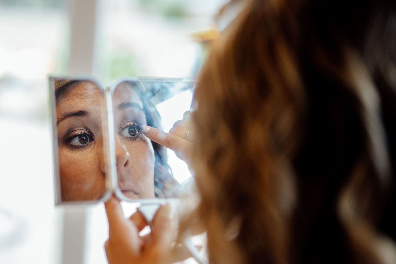 Close-up reflection of someone applying makeup in a small mirror.