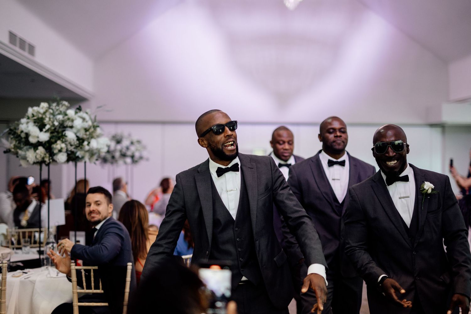 Wedding party in formal black attire stands in line at elegant indoor venue.