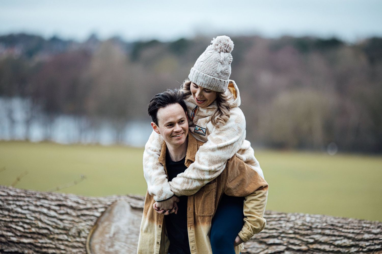A playful couple sharing a romantic moment on a fallen tree trunk in a field.
