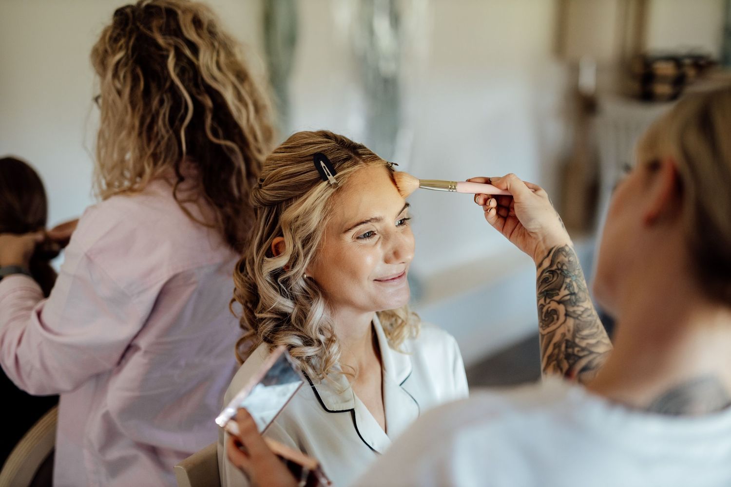 Bridesmaids in pink robes get their hair styled during wedding preparations.